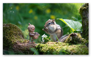 A Becorn holding a basket of sunflower seeds is standing on a mossy log next to a chipmunk that is eating a seed.