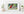 The photo of a Becorn and a cardinal in a thin, white frame on a white shelf against a white wall. On either side of it are potted plants and a small stack of books. In the lower right corner of the print’s white border is David Bird’s signature.